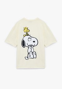 Creme T-shirt med en sort kontur tegneserie design af Snoopy med Woodstock siddende på hans hoved. Korte ærmer og afslappet pasform.