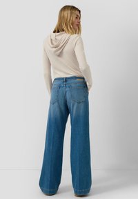 Hellbeige gerippter Hoodie mit Kapuze auf der Rückseite, kombiniert mit weit geschnittenen, verwaschenen blauen Denimjeans in mittlerer Waschung und fünf Taschen.