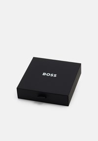 Scatola rettangolare nera con texture liscia, dotata di un logo "BOSS" argentato sulla parte superiore e di una piccola linguetta per l'apertura.