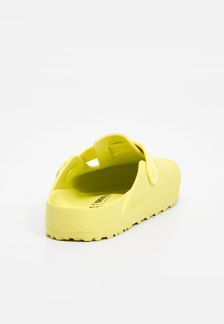 Gelbe Clogs aus strukturiertem Gummi mit einem hinteren Riemen und einer dicken, robusten Sohle. Verfügt über Belüftungslöcher für Atmungsaktivität.