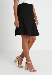 Gonna nera a campana con una texture liscia, di lunghezza al ginocchio, con dettagli di cucitura discreti. Abbinata a sandali nudi con tacco blocco.