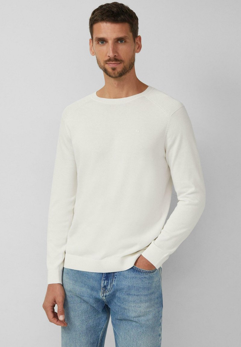 Lichtbeige trui met een ronde hals, ribbelmanchetten en -zoom. Gekocht met lichtblauwe jeans, met een subtiele logo op de borst.