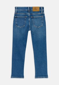Jeans en denim bleu avec un design à jambes droites, style cinq poches, et une étiquette de marque beige cousue sur la taille à l'arrière.