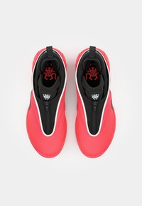 Røde og sorte atletiske sko med en glat overdel, lynlåslukning og en karakteristisk logo på indersålerne. Rund tå og polstret sål.