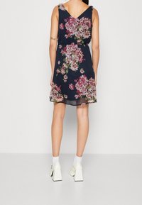 Blommig klänning i marinblått med rosa och vita blommor, ärmlös design, rynkad midja och längd över knäna. Bärs med kraftiga vita klackar.