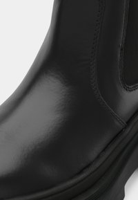 Gros plan de la tige en cuir noir lisse et de la semelle d'une botte Chelsea, montrant une couture détaillée et un panneau latéral élastique.