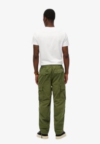 Groene cargobroek met meerdere zakken, een elastische tailleband en taps toelopende benen, gecombineerd met een eenvoudig wit T-shirt en zwarte schoeisel.