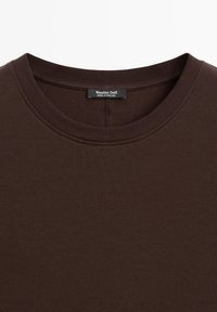 T-shirt girocollo di colore marrone scuro con cuciture visibili e una piccola etichetta nera con la scritta "Massimo Dutti Made in Portugal" sul collo.