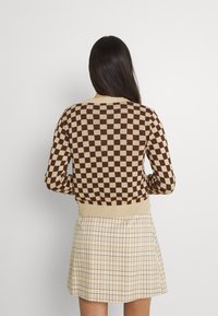Braun- und cremefarbener karierter Pullover mit geripptem Saum und Bündchen, kombiniert mit einem beigen karierten Rock mit feinen Linien und einem ausgestellten Design.