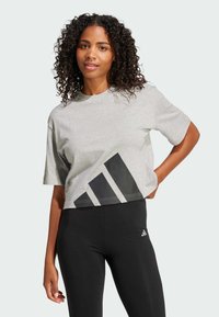 Siva skraćena majica s crnim dizajnom tri pruge na dnu, kratkim rukavima i okruglim izrezom, u kombinaciji s crnim tajicama.