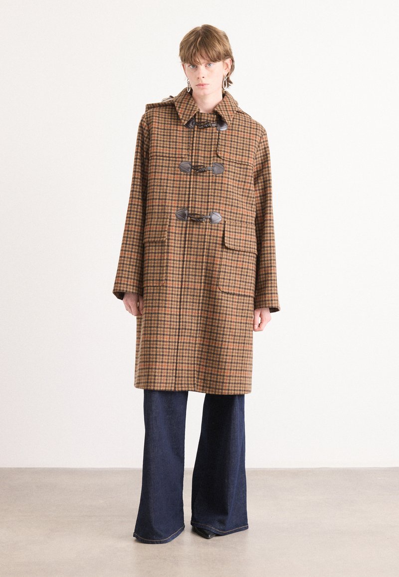 Bruine geruite trenchcoat met een capuchon, voorzien van grote zakken, togglesluitingen en een losse pasvorm. Gecombineerd met wijde, donkere spijkerbroeken.