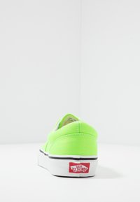 Kirkkaan vihreä Vans-tenniskenkä nähtynä kannasta, jossa on valkoinen pohja ja punainen 'Vans Off The Wall' -logo yksinkertaisella valkoisella taustalla.