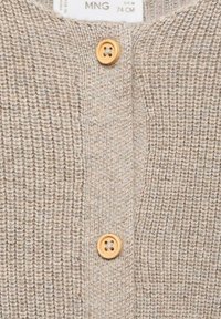 Beigefärgad stickad kofta med ett strukturerat mönster. Har träknappar och rund hals. Mjuk, varm material; avslappnad design.