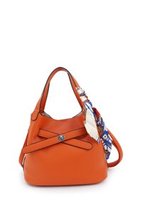 Oranje leren handtas met textuur en een gebogen vorm, voorzien van een decoratieve sjaal die aan de handgreep is geknoopt en een zilveren ronde sluiting.