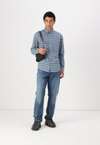 Plaid button-up shirt in blue tones, denim jeans, and black crossbody bag. Black sneakers with textured sole. Plain background.