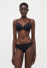 Ensemble de lingerie noire comprenant un soutien-gorge rembourré avec des bordures en dentelle et un string assorti, en tissu lisse, avec des bords festonnés.