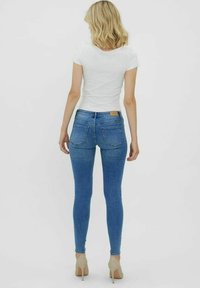 Skinny blue jeans made of denim, featuring a mid-rise waist, two back pockets, and a tan leather tag above the right pocket.