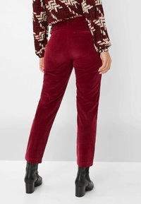Rote Cordhose mit geradem Bein, ausgestattet mit einer Gesäßtasche und kombiniert mit schwarzen Knöchelschuhen. Weicher Stoff und glatte Oberfläche.