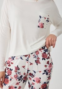 Λευκό μπλουζάκι μακρύ μανίκι με τσέπη με λουλούδια; μαλακό ύφασμα. Συνδυασμένα παντελόνια με λευκή βάση και κόκκινο και μπλε λουλουδάτο μοτίβο.