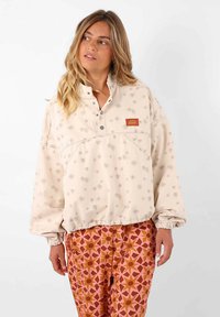 Pull beige avec motif flocon de neige et col à boutons. Manches et ourlet élastiques, associé à un pantalon rose et orange à motifs.