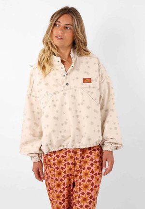 Pull beige avec motif flocon de neige et col à boutons. Manches et ourlet élastiques, associé à un pantalon rose et orange à motifs.