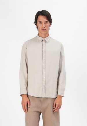 Camisa de manga larga color beige claro con cuello abotonado, tejido texturizado y un patrón sutil, combinada con pantalones marrón claro.