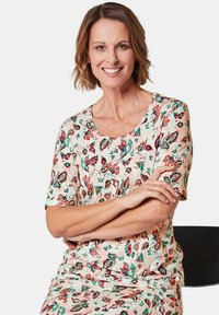Floral print top in soft, lightweight fabric features a round neckline, short sleeves, and a pastel peach background with red and green accents.