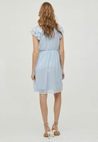 Ljusblå klänning med prickar, volangärmar, elastisk midja och genomskinlig foder vid nederkanten. Bärs med guldiga sandaler med remmar.