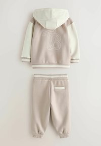 Dwuczęściowy dres składający się z beżowej bluzy z kapturem z białymi akcentami i haftowanym wzorem "TB", w zestawie z dopasowanymi, zwężanymi spodniami.