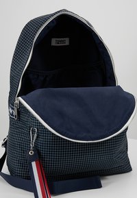 Marinblå ryggsäck med rutmönster, dragkedjestängning och en stor öppning. Har ett accentband i röd, vit och blå. Insidan är mörkblå.