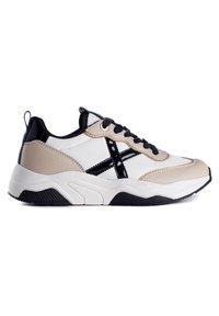 Sneaker with a white and beige synthetic upper, black accents, textured sole, and contrast stitching. Features a rounded toe and lace closure.
