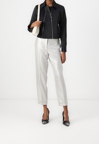 Veste noire courte avec fermeture éclair argentée, associée à un pantalon droit argenté brillant. Talons hauts noirs complètent la tenue.