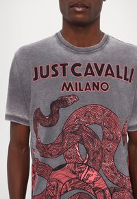 Grijze t-shirt met korte mouwen met een opvallende rode slangafbeelding en "JUST CAVALLI MILANO" tekst in vet zwart. Zachte katoenmateriaal.