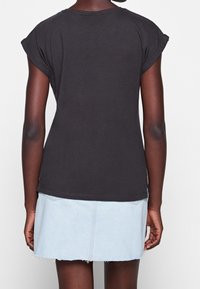 Černé tričko s krátkým rukávem a ohrnutými manžetami, spárované se světle modrou džínsovou sukní s třepícími se okraji a jemnými designovými liniemi.