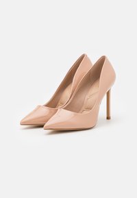 Korkeat nuden väriset patenttijanat, joissa on terävä kärki ja ohut stiletto-korko. Suora pinta ja minimalistinen muotoilu.
