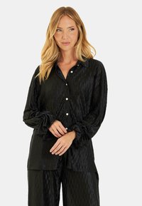 Camisa negra de botones con tejido texturizado y patrón acanalado, que presenta puños fruncidos y un cuello clásico.