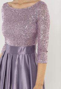 Lila Paillettenoberteil mit Dreiviertelärmeln, kombiniert mit einem satinfarbenen Lavendelkilt mit Falten, der ein strukturiertes Design schafft.