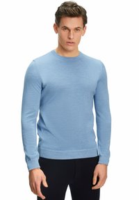 Pull à manches longues bleu clair en tissu doux et texturé. Il a un col ras du cou et des poignets ajustés, associé à un pantalon sombre.