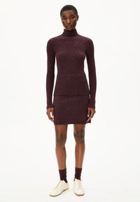 Bordeauxfarbenes, geripptes Strickkleid mit hochgeschlossenem Hals, langen Ärmeln und eng anliegendem Rock. Kombiniert mit cremefarbenen Schuhen und dunklen Socken. Texturiert.