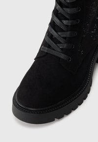 Black ankle boot with a suede upper, textured lace detailing, and a chunky rubber sole. Features black laces and a round toe design.