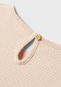 Ljusrosa texturerad topp med en nyckelhålsöppning bak, fäst med en rund träknapp. Subtil räfflad mönstring synlig.