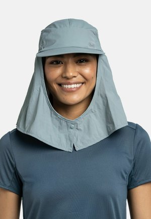 Persona sonriente que lleva un sombrero de sol azul claro con protección para el cuello y una camisa azul oscuro de manga corta sobre un fondo liso.