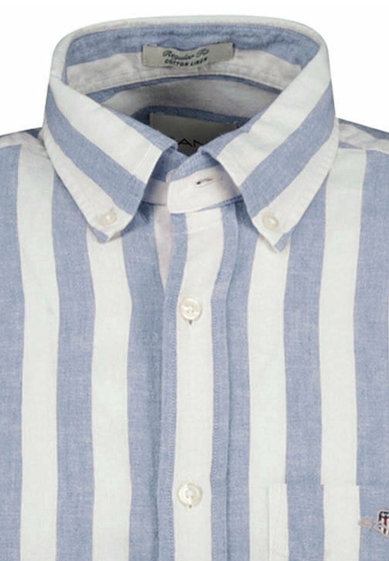 Camicia a righe con bottoni in cotone leggero e lino. Presenta strisce verticali alternate azzurro chiaro e bianco, una tasca sul petto e un colletto appuntito.
