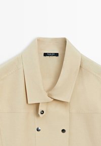 Beige collared jacket with black snap buttons and a visible brand label "Massimo Dutti" inside the collar.
