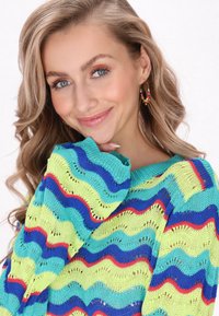 Maglione con un design ondulato in tessuto di maglia verde, blu e rosso. Presenta una vestibilità ampia e un collo a coste, che mette in evidenza una trama a tessitura aperta.
