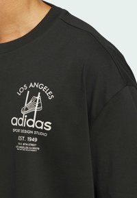 Zwart katoenen t-shirt met een witte grafische print met tekst en een illustratie van een sneaker. Klassieke ronde halslijn en korte mouwen.