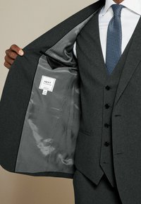 Szary garnitur w dopasowanym kroju z gładką szaro-skalną podszewką, z guzikami i metką z napisem "NEXT Tailoring Slim Fit."