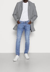Šedý vlněný kabát, bílý tričko, světle modré skinny džíny a bílé tenisky. Kabát má zapínání na knoflíky a hladkou texturu.