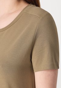 T-shirt vert olive à manches courtes en tissu doux et extensible ; col rond ; texture à côtes fines ; couture soignée le long des coutures.