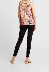 Pastellinpunainen kukallinen hihaton toppi, jossa on v-muotoinen selkäosa, yhdistetty mustiin kapeisiin housuihin ja nudenvärisiin paksukorkoisiin sandaaleihin.